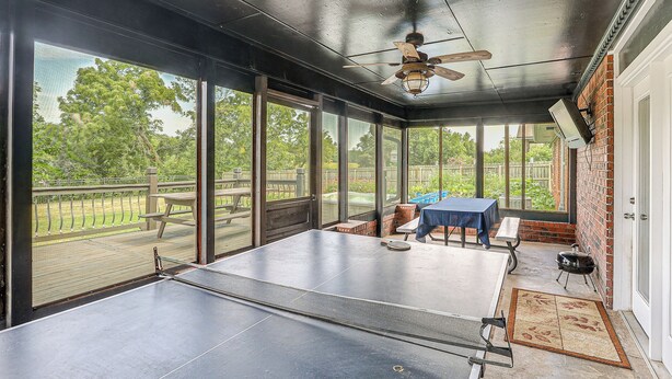 A sunroom with a ping pong table, large windows, and a ceiling fan. - Waterfront Kansas Home w/ Private Fire Pit! (Arkansas City)