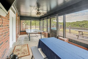 A covered patio with a ping pong table, a bench, and a view of a park.