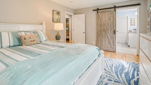 Une chambre à coucher comprenant un lit, un ventilateur de plafond, une porte donnant sur une salle de bain et une vue sur cette dernière.