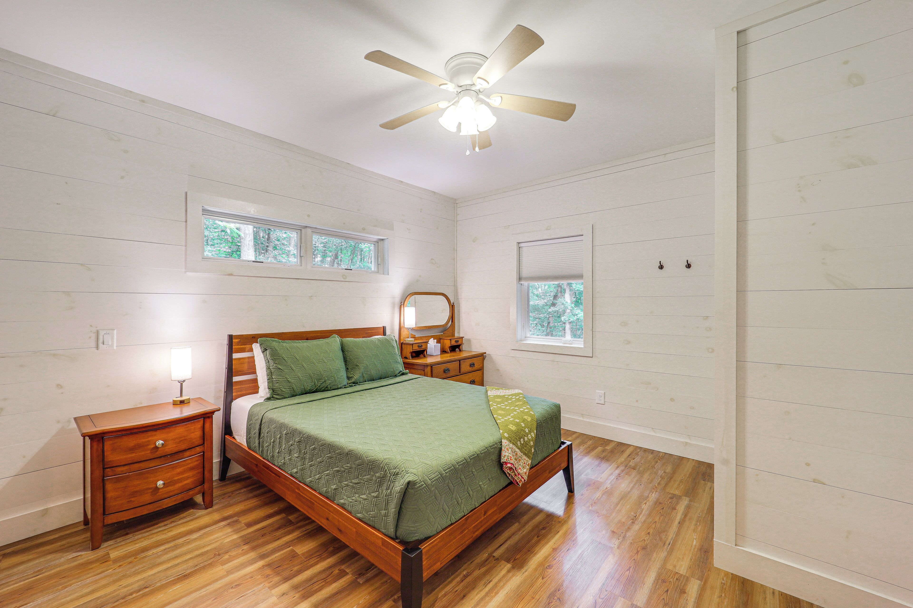 Une chambre à coucher avec un lit en bois, deux tables de chevet, un ventilateur de plafond et deux fenêtres.