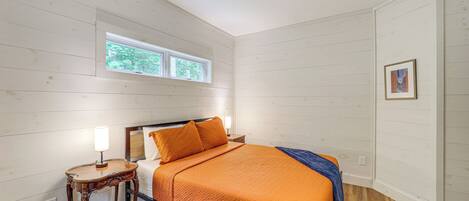 A bedroom with a bed, a bedside table with a lamp, a ceiling fan, a window, and a door.