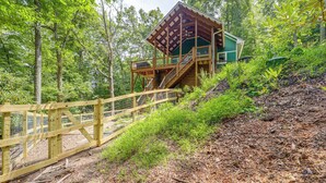 Una cabaña de madera con balcón y escaleras, rodeada de un bosque denso.