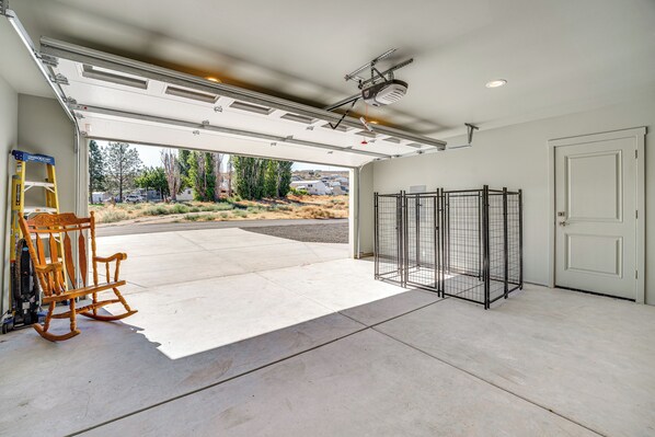 Un garage avec un sol en béton, une chaise berçante en bois, un portail en métal et une vue sur un quartier résidentiel.
