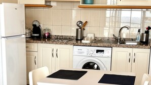 A modern kitchen with white cabinets, a built-in washing machine, a sink, and a dining area with a table and chairs.