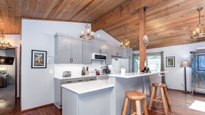 A modern kitchen with grey cabinets, a white island, wooden stools, and pendant lighting. - Timb07 - Great for Families, Hot Tub, AC, Foosball (Sunriver)
