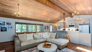A spacious living area with a large L-shaped sectional sofa, a round coffee table, and a kitchen area with modern appliances. - Timb07 - Great for Families, Hot Tub, AC, Foosball (Sunriver)