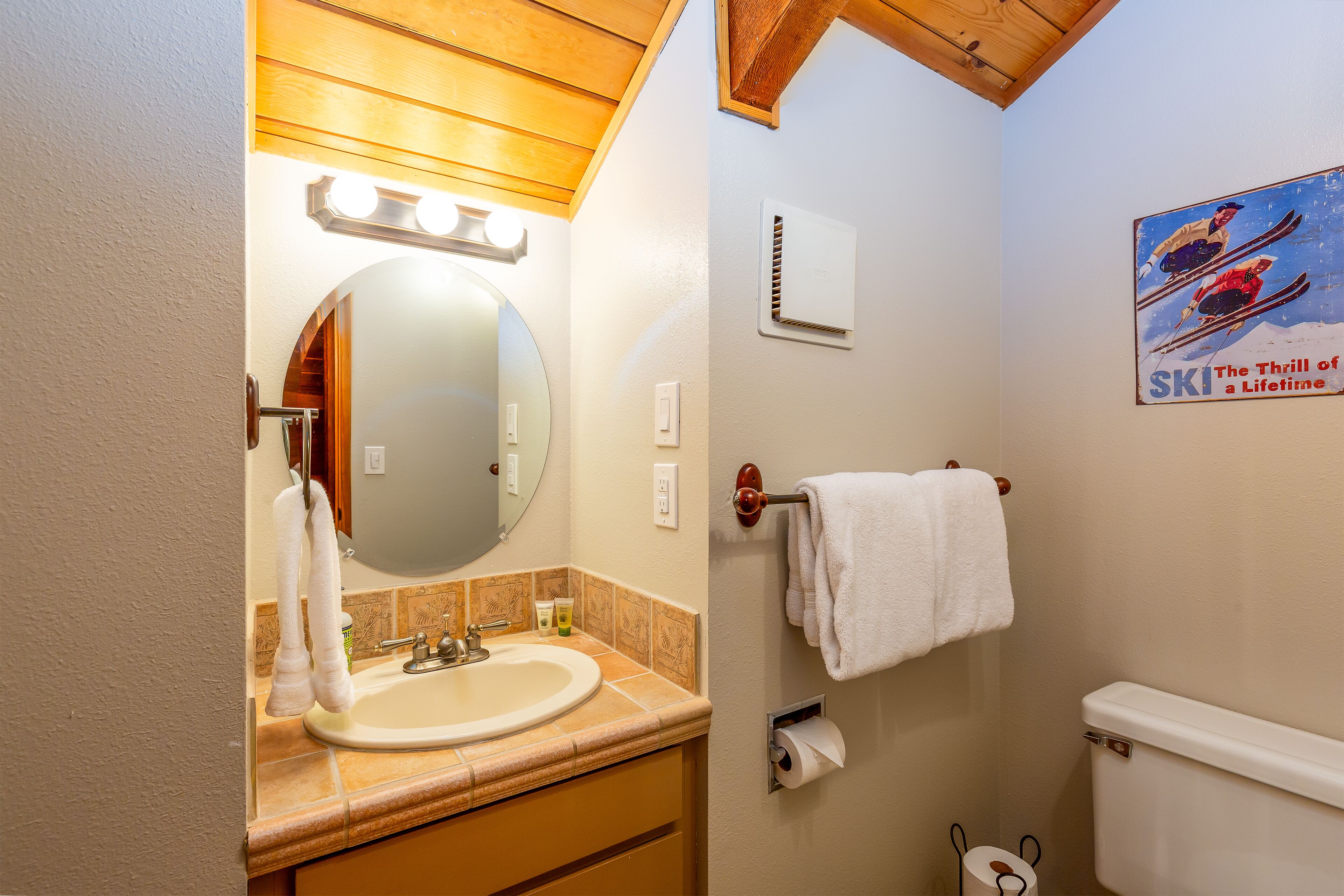 Une salle de bain équipée d’un lavabo, d’un miroir, d’un porte-serviettes, de toilettes et d’une affiche accrochée au mur.