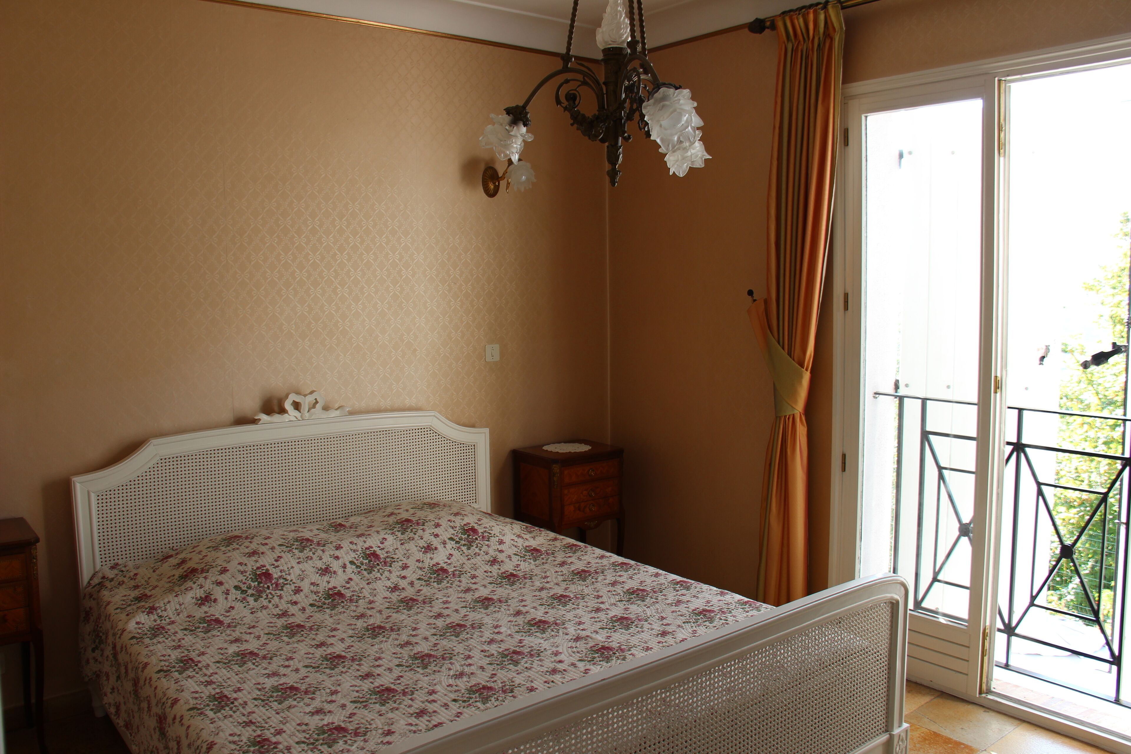 Une chambre à coucher comprenant un lit, une table de chevet, une commode, un lustre et un balcon avec une balustrade.