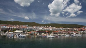 Una cittadina costiera con un porto turistico, edifici dai tetti rossi e uno sfondo collinare.