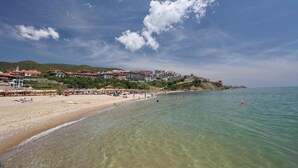 Una spiaggia con acque limpide, una riva sabbiosa e edifici sullo sfondo.