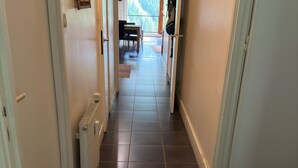 A narrow hallway with tiled flooring, a radiator, and a door leading to a balcony with a table and chairs.