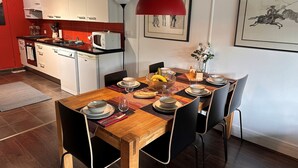 A modern kitchen with white cabinets, a red pendant light, and a dining area with a wooden table set for four.