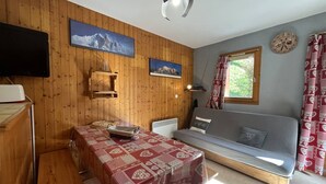 A cozy room with wooden walls, a dining table with a red and white tablecloth, a sofa, a television, and a window with curtains. - Cozy 2-Room Apt for 6 with Terrace, Ski Access, Pet-Friendly, Central Location in Plan Peisey (Peisey-Nancroix-Plan Peisey)