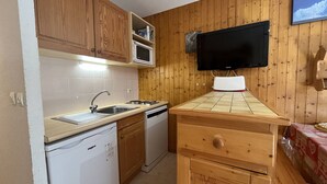 A compact kitchen with wooden cabinets, a microwave, a sink, a dishwasher, and a television mounted on the wall. - Cozy 2-Room Apt for 6 with Terrace, Ski Access, Pet-Friendly, Central Location in Plan Peisey (Peisey-Nancroix-Plan Peisey)