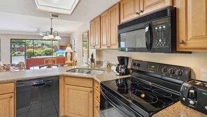 A modern kitchen with wooden cabinets, a built-in microwave, a stovetop, and a dishwasher. - A-108 - Resort View and Corner Unit (Naples)