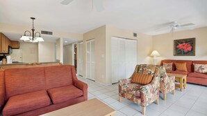 A living room with a red sofa, floral armchairs, a wooden coffee table, and a ceiling fan. - A-108 - Resort View and Corner Unit (Naples)