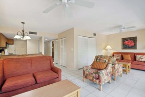A living room with a red sofa, floral armchairs, a wooden coffee table, and a ceiling fan. - A-108 - Resort View and Corner Unit (Naples)
