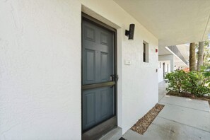 A white exterior wall with a dark grey door, a small window, and a number '108' sign. - A-108 - Resort View and Corner Unit (Naples)