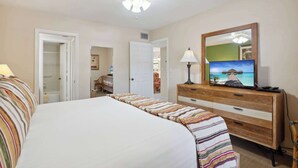 A hotel room with a bed, a dresser, a television, and a door leading to another room. - A-108 - Resort View and Corner Unit (Naples)