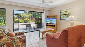 A living room with a sofa, a table, a TV, and a ceiling fan. - A-108 - Resort View and Corner Unit (Naples)