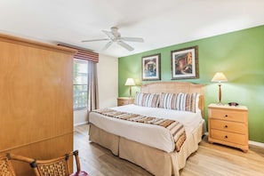 A bedroom with a bed, bedside tables, a chair, a ceiling fan, and artwork on the wall. - B-212 - Second Floor Lake View & Sleeps 6 (Naples)