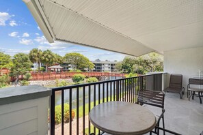 Un balcon avec une table et des chaises, donnant sur un jardin et un plan d’eau.