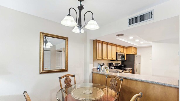 A dining area with a glass table and wooden chairs, a kitchen with wooden cabinets and stainless steel appliances, and a ceiling light fixture. - B-212 - Second Floor Lake View & Sleeps 6 (Naples)