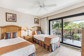 A hotel room with two beds, a ceiling fan, a balcony with a table and chairs, and framed artwork on the walls.