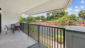 A balcony with a pergola, outdoor seating, and a view of a park with trees and a fence. - B-212 - Second Floor Lake View & Sleeps 6 (Naples)