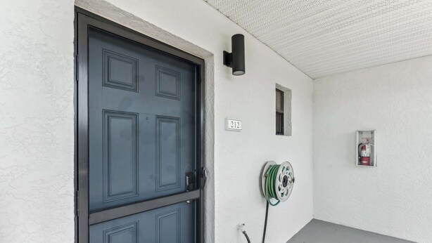 A hallway with a dark blue door, a wall-mounted fire extinguisher, and a coiled cable. - B-212 - Second Floor Lake View & Sleeps 6 (Naples)