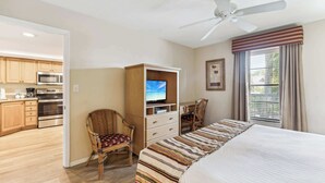 A hotel room with a bed, a TV, a desk, and a chair. There is a kitchenette in the background. - B-212 - Second Floor Lake View & Sleeps 6 (Naples)