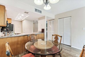 A dining area with a glass table and chairs, a wooden counter, and a kitchen in the background. - B-212 - Second Floor Lake View & Sleeps 6 (Naples)