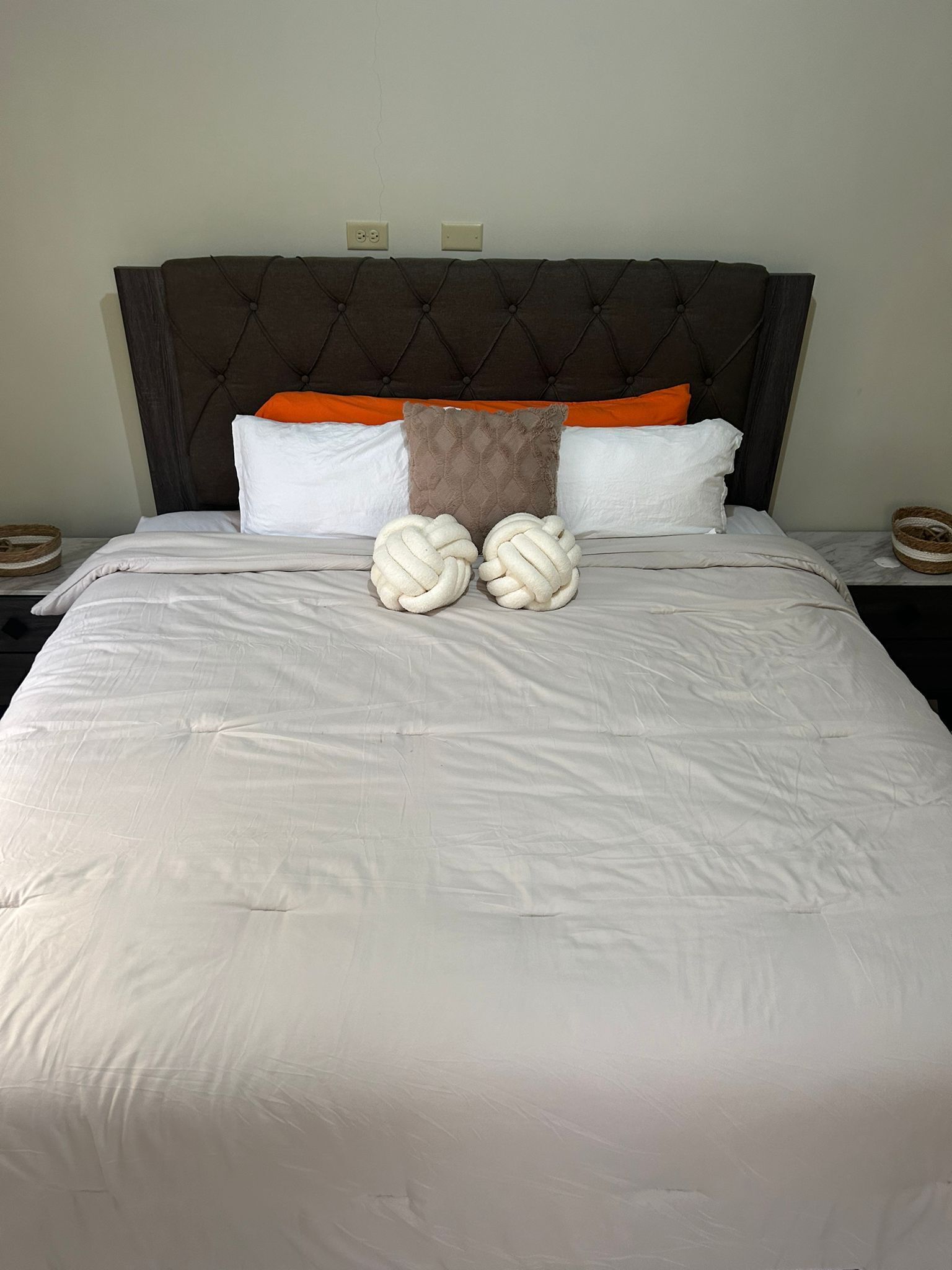 A neatly made bed with white linens, a tufted headboard, and decorative pillows.