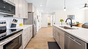 A modern kitchen with stainless steel appliances, light wood flooring, and a central island with a sink. - Adventure Alcove: Desert Color Lagoon + Beaches (St. George)
