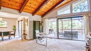 Une pièce spacieuse avec un plafond haut, une grande porte-fenêtre coulissante donnant sur une terrasse extérieure, un coin repas avec une table et des chaises, et un coin salon avec un canapé et une lampe.