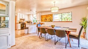 Une cuisine moderne avec des meubles blancs, un coin repas doté d’une grande table et de chaises, et une fenêtre donnant sur un paysage verdoyant.