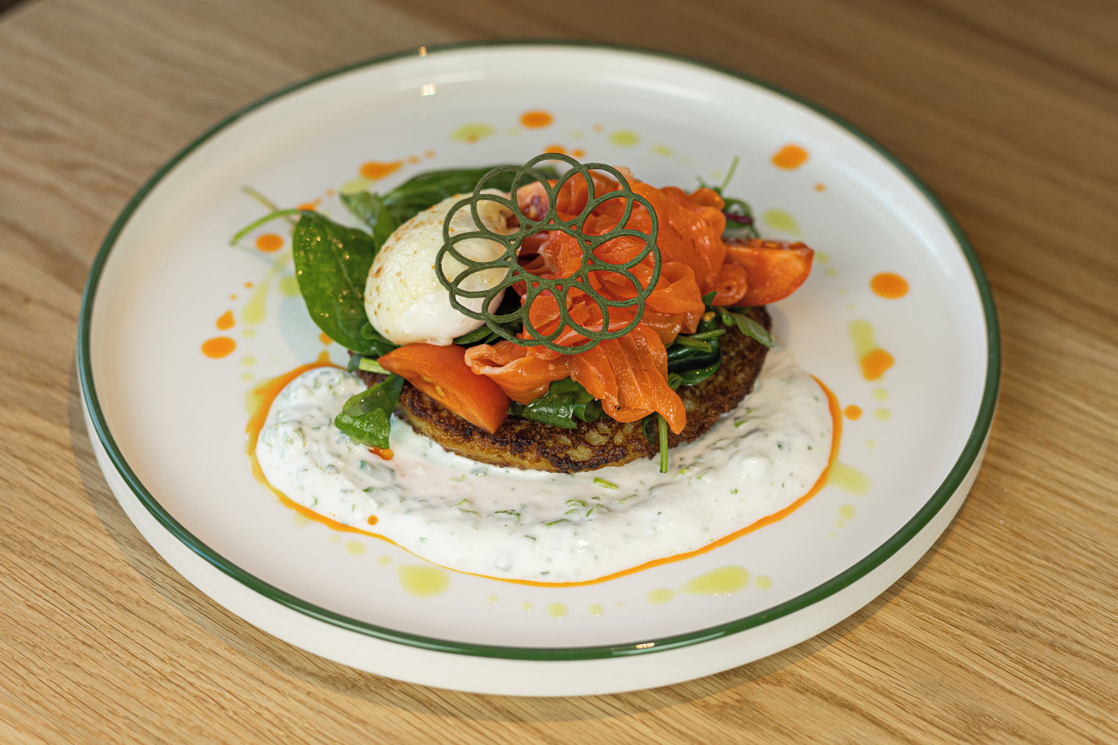 A plate of food with a green rim, containing a slice of bread topped with greens, a poached egg, and smoked salmon, accompanied by a creamy sauce.