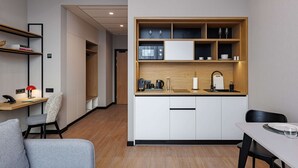 A compact kitchen with white cabinets, a wooden countertop, and a built-in shelf with kitchenware.