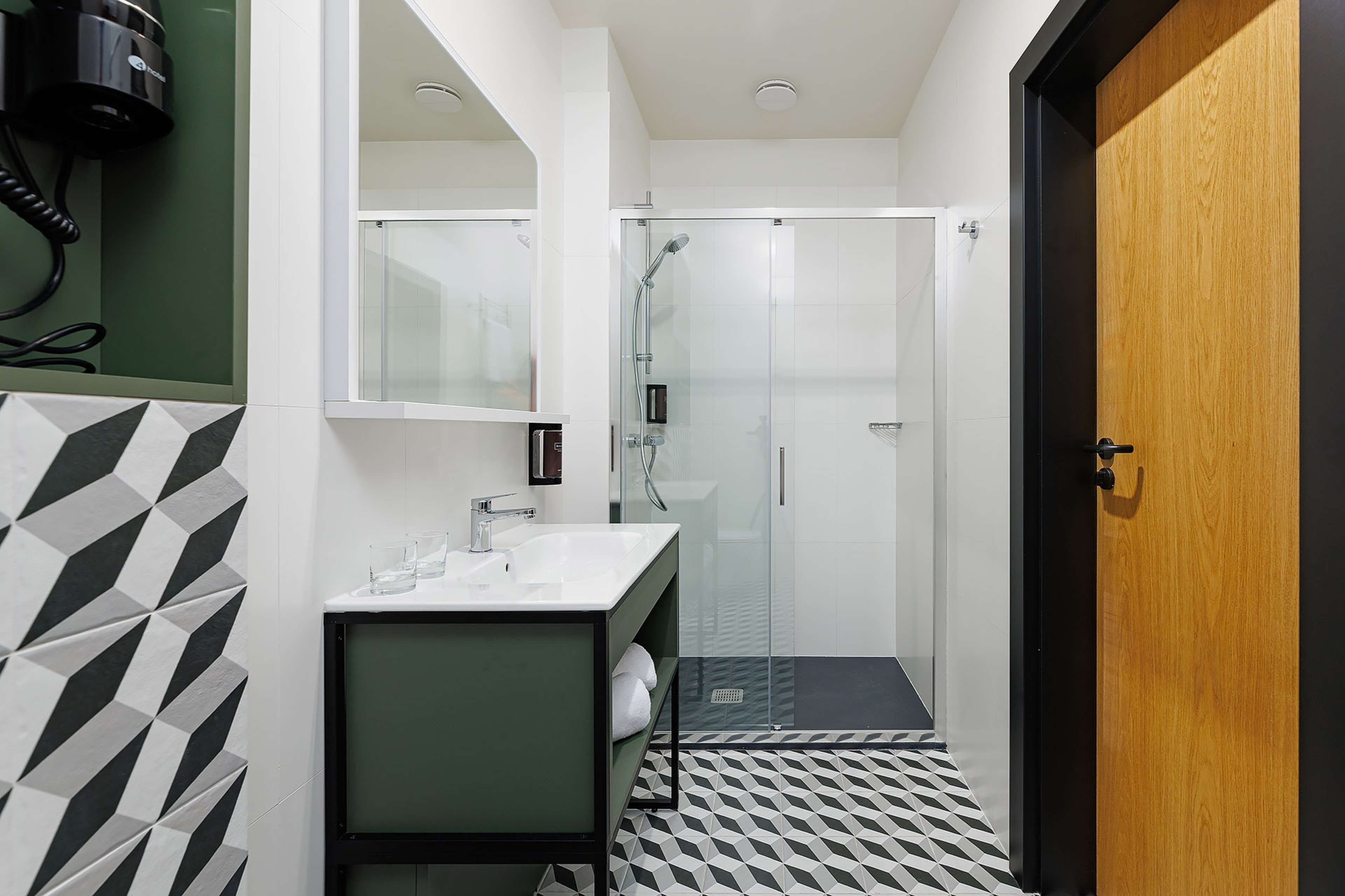 A modern bathroom with a glass shower enclosure, a white sink, and a wooden door.