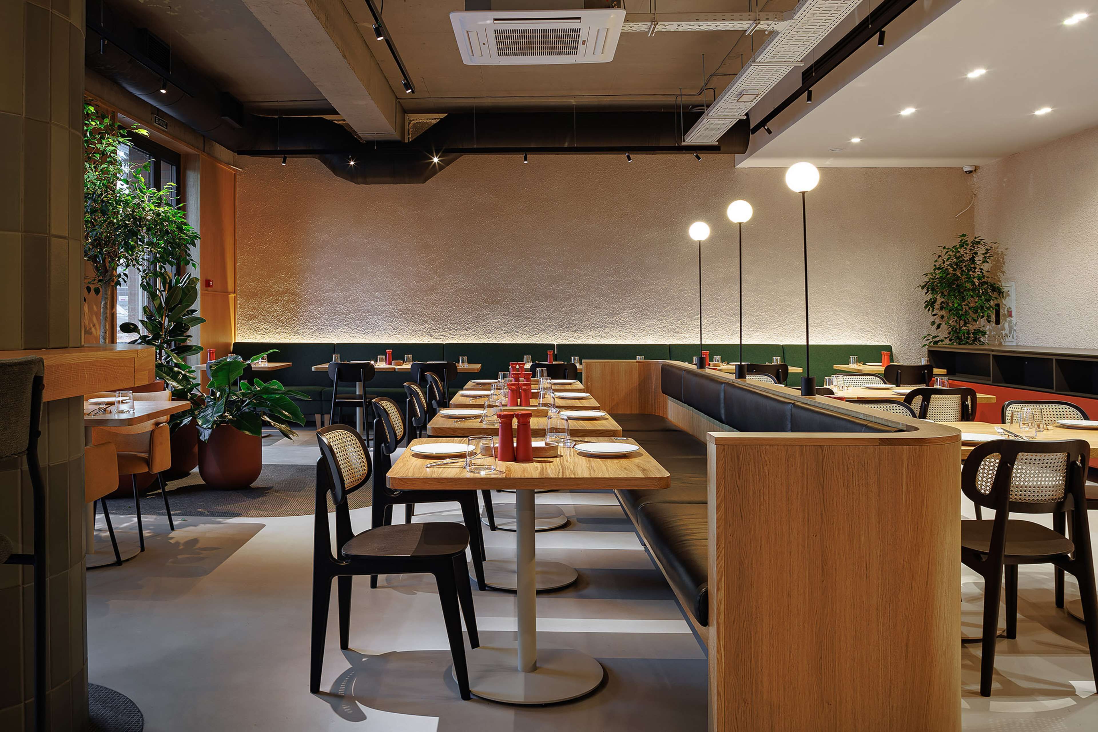 Ein modernes Restaurant mit langen Gemeinschaftstischen, einzelnen Sitzecken und Topfpflanzen.