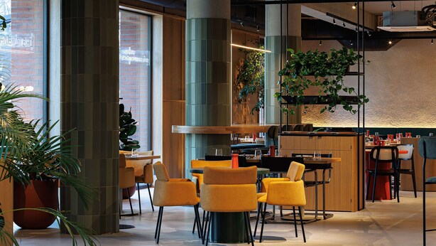 A modern interior with high ceilings, large windows, and a mix of seating arrangements including tables and chairs.