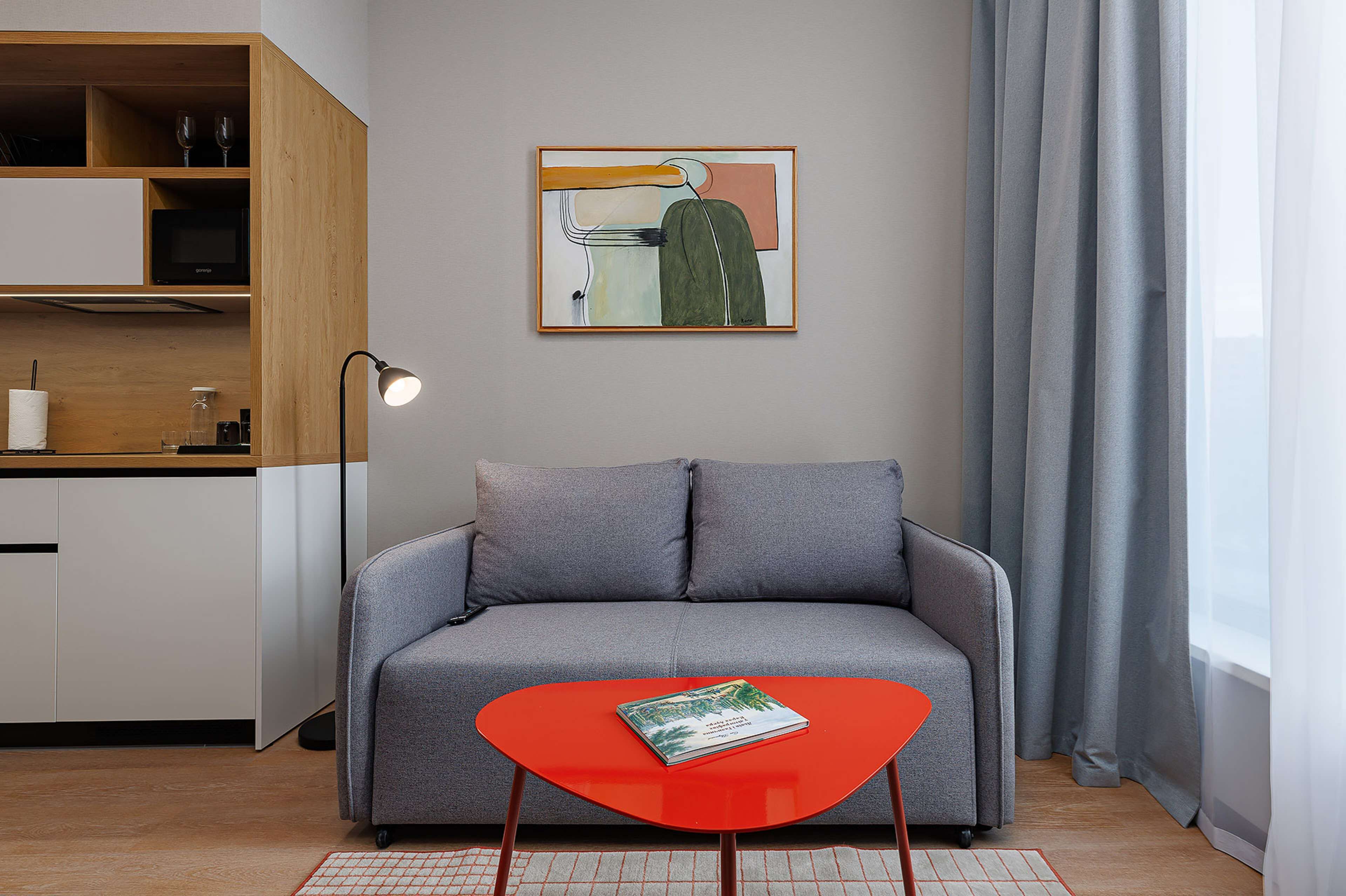 A modern living room with a grey sofa, a red coffee table, and a painting on the wall.