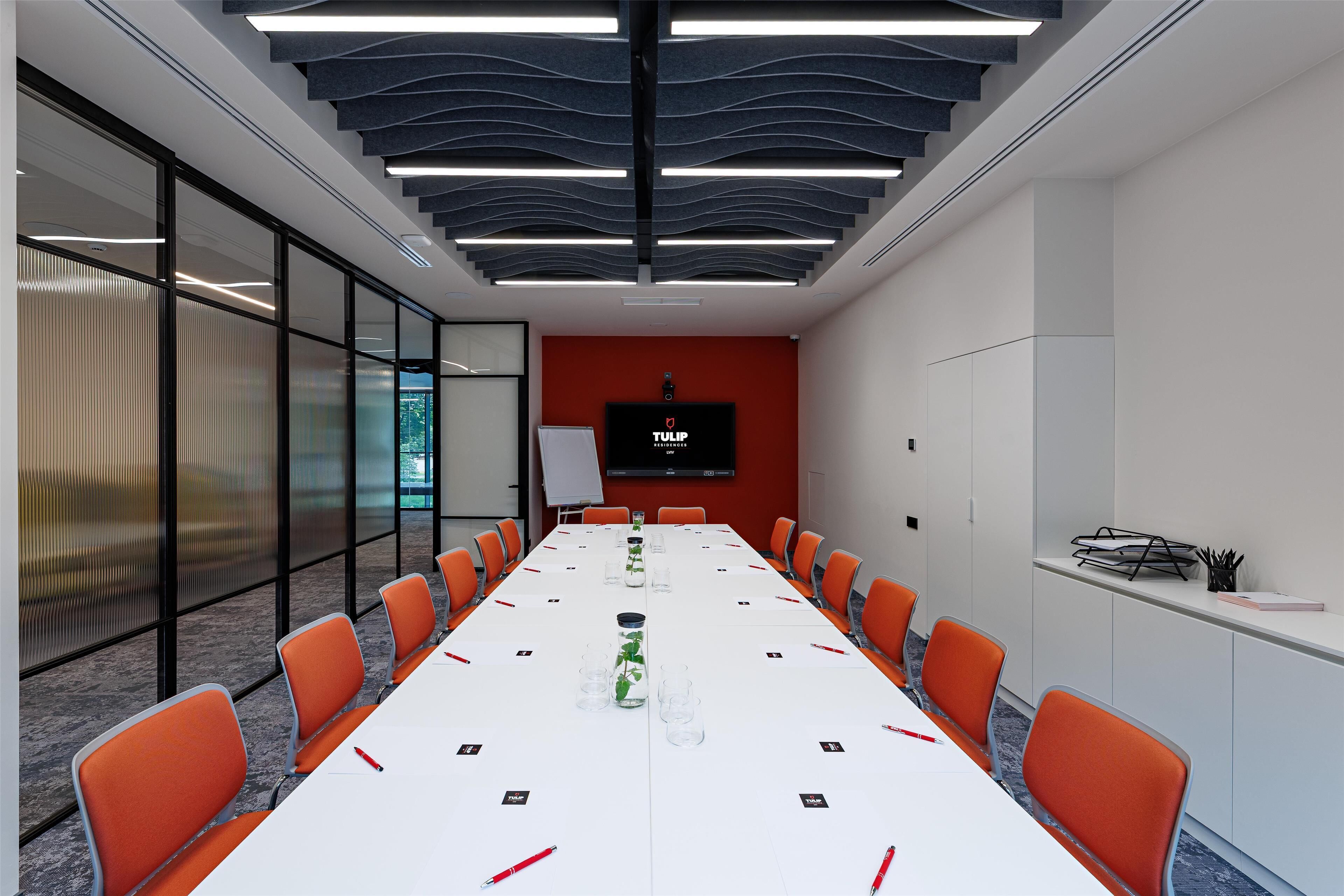 A conference room with a long table, orange chairs, a whiteboard, and a screen displaying 'TULIP'.
