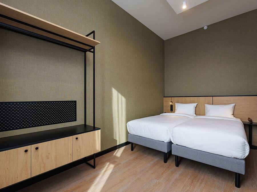 Una habitación de hotel moderna con cama, escritorio y televisor montado en la pared.