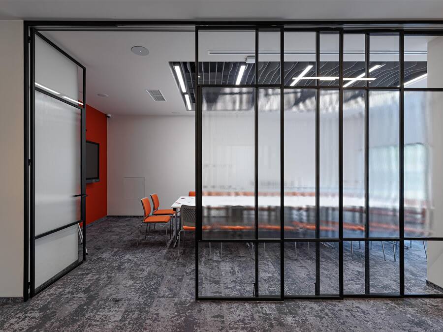 A modern meeting room with a glass partition, a conference table, and orange chairs.