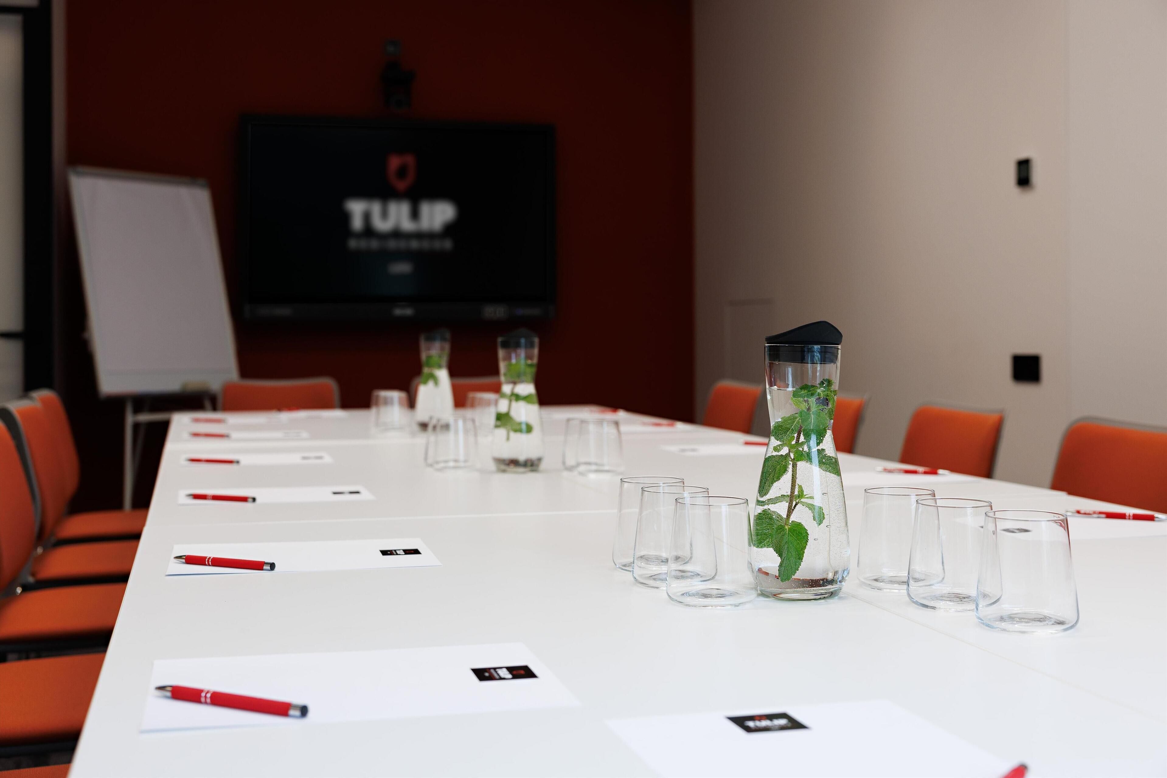 A conference room with a long table, chairs, and a TV screen displaying 'TULIP'.