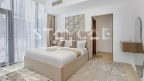 A modern bedroom with a large bed, a bedside table, a mirror, and a view of the outdoors. - Staycae- National Bonds Residences  (Dubai)