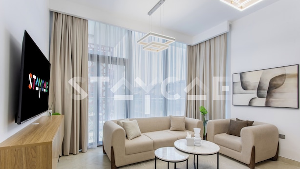 A modern living room with a beige sofa, a coffee table, and a TV on a wooden stand. - Staycae- National Bonds Residences  (Dubai)