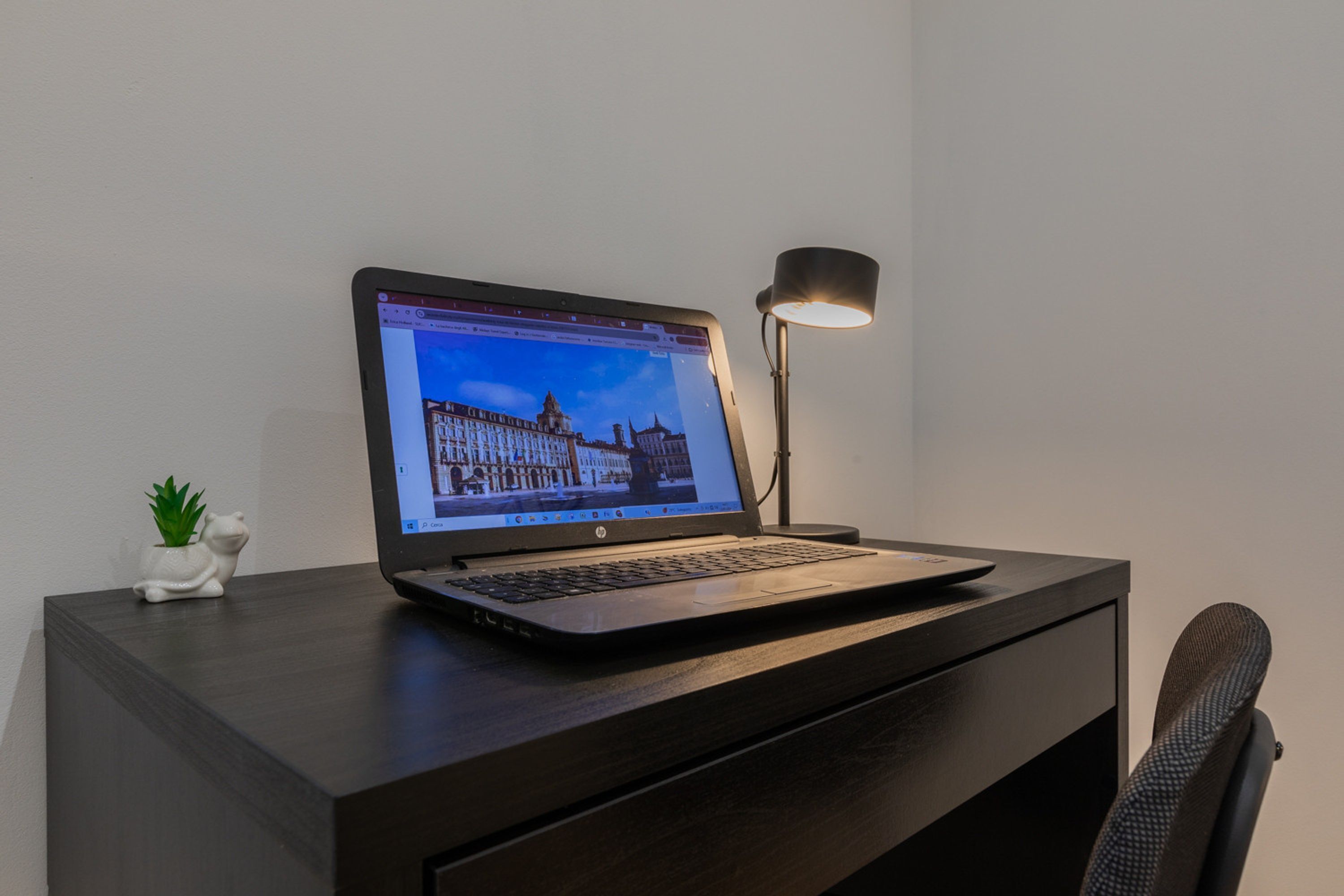 A laptop on a dark wooden desk with a lamp, a small plant, and a chair.