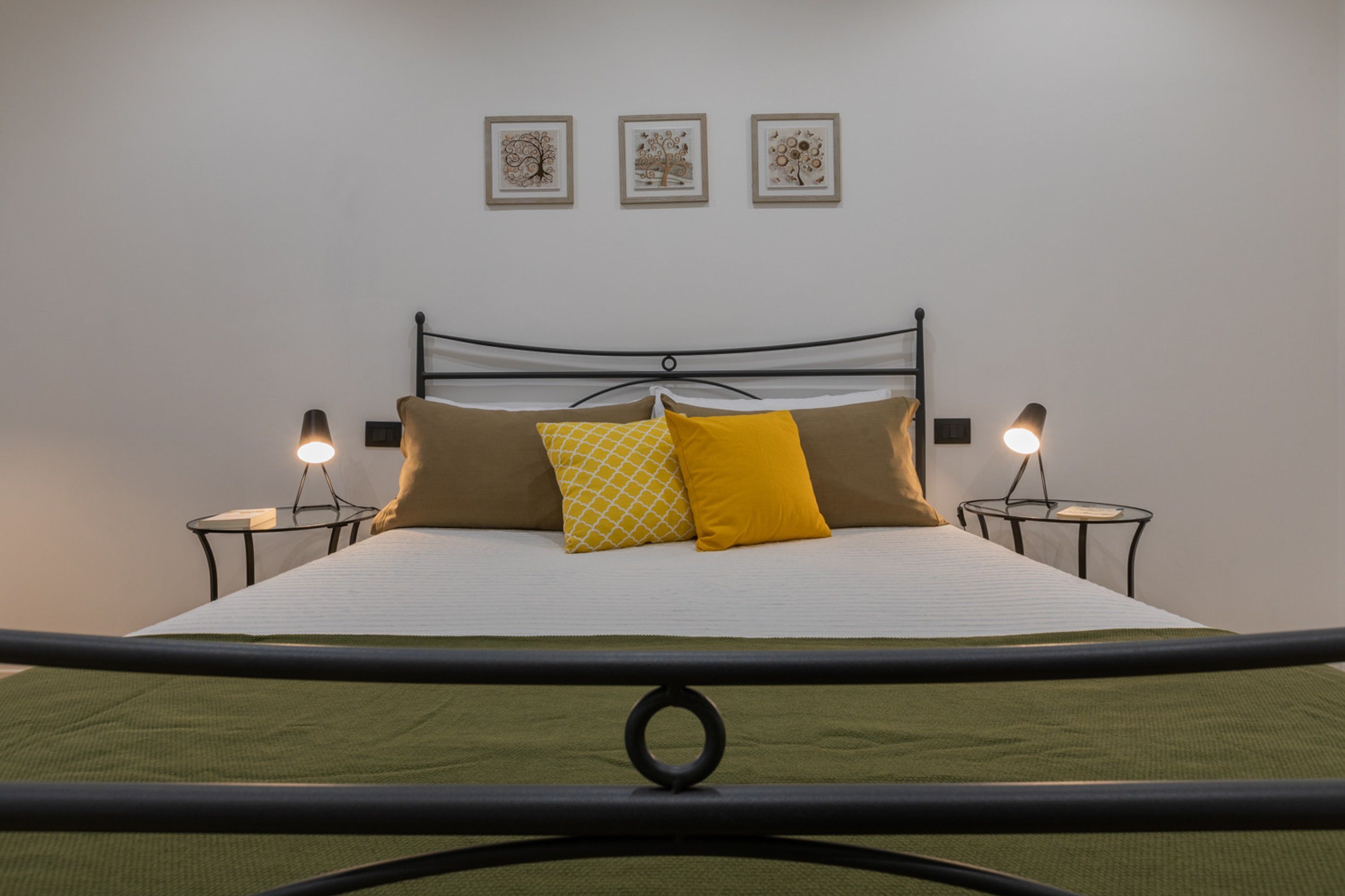 A neatly made bed with a white and green bedspread, two bedside tables with lamps, and three framed pictures on the wall.